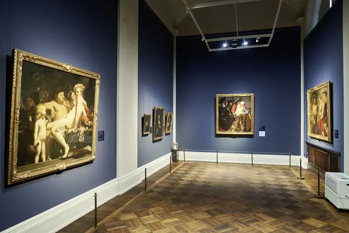 Eine Ausstellungsansicht mit zahlreichen Gemälden an den Wänden. 