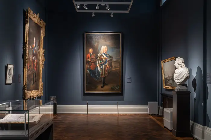 Ein kleiner Ausstellungsraum mit Gemälden und einer Büste