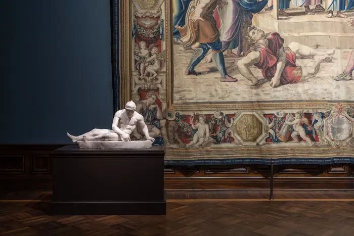 Ein Ausstellungsraum mit einer Marmorstatue und einem Wandteppich 