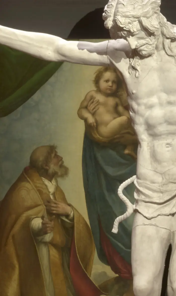 Ein Kruzifix vor dem Gemälde "Sixtinische Madonna" von Raffael