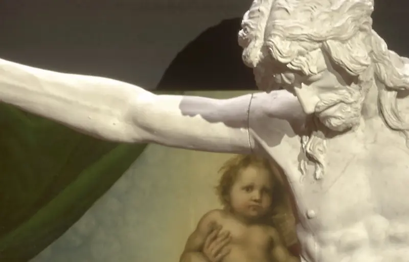 Ein Kruzifix vor dem Gemälde "Sixtinische Madonna" von Raffael