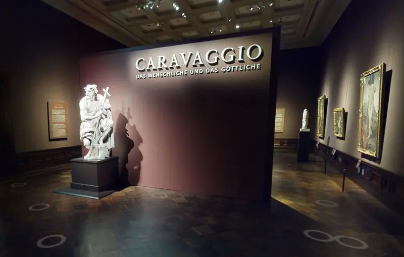 Eine Ausstellungsansicht mit Gemälden und einer Statue