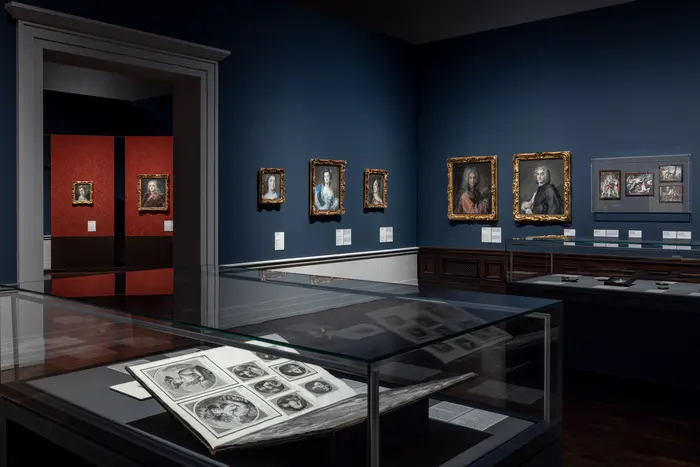 Eine Ausstellungsansicht mit Gemälden und Vitrinen 