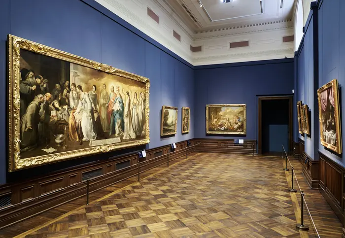 Eine Ausstellungsansicht mit zahlreichen Gemälden an den Wänden. 