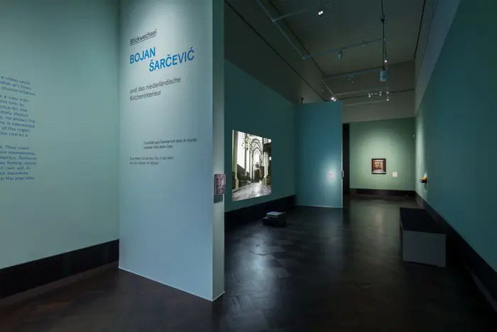 Ausstellungsansicht einer Videoarbeit des Künstlers Bojan Šarčević mit Gemälden niederländischer Kircheninterieurs im abgedunkelte Semperkabinett